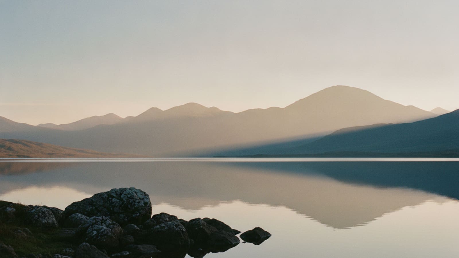 A still highland loch at first light, mountains mirrored in mirror-flat water