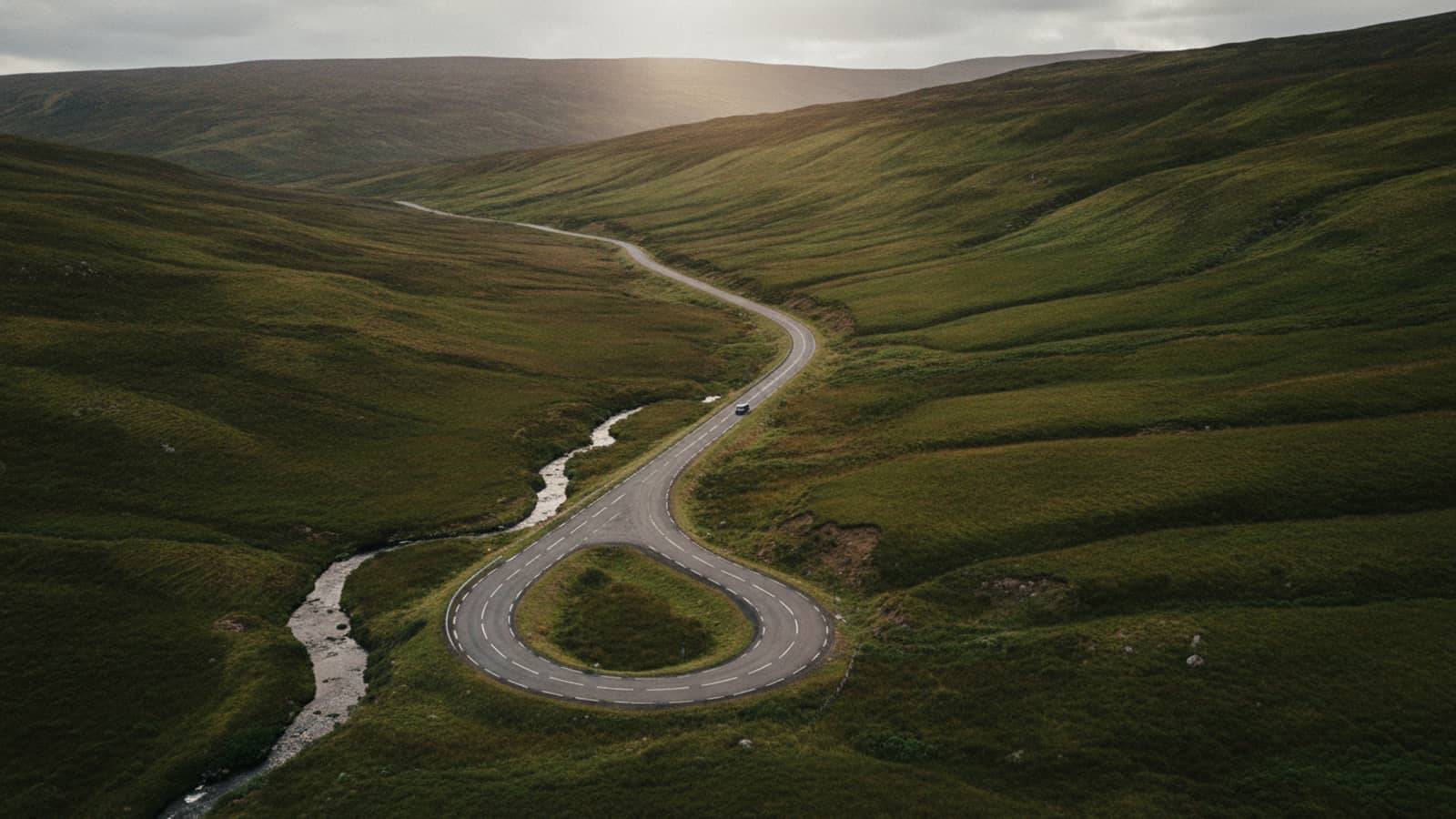 A single-track road winding through a Scottish highland glen at first light